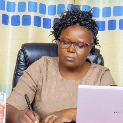 Hellen, DEN Board Chairperson, seated at her desk, writing in a notebook